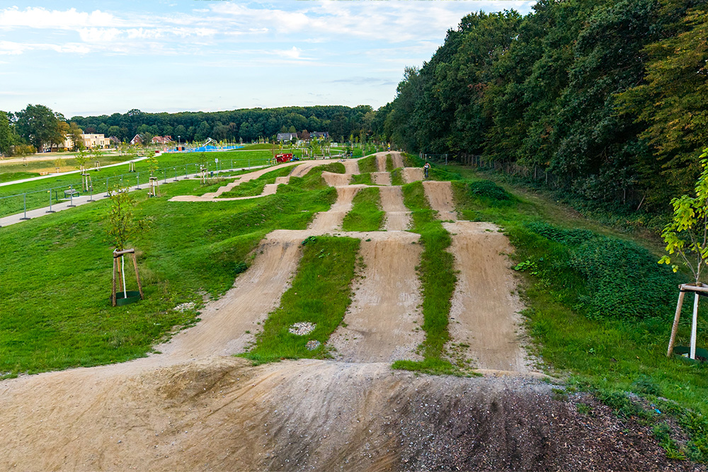 Dirt-Bike-Strecke mit mehreren Erdhügeln und Sprüngen in einer begrünten Parkanlage