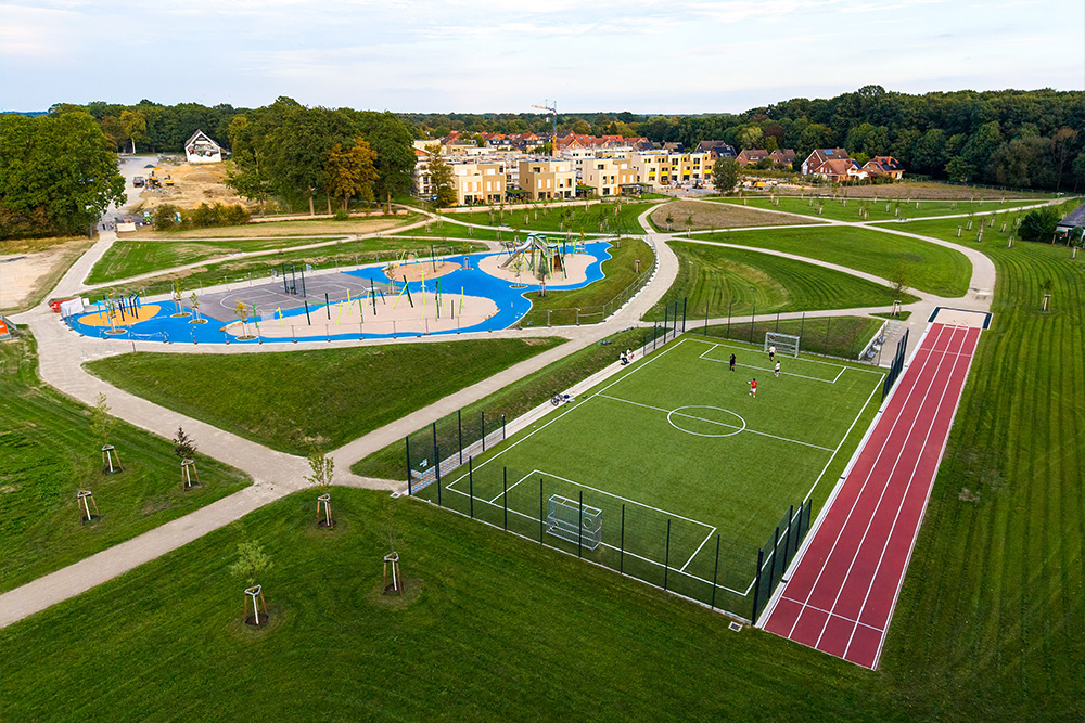 Luftaufnahme des Landschaftsparks mit Spielplatz, Fußballplatz, Laufbahn, Spazierwegen und angrenzender Wohnbebauung