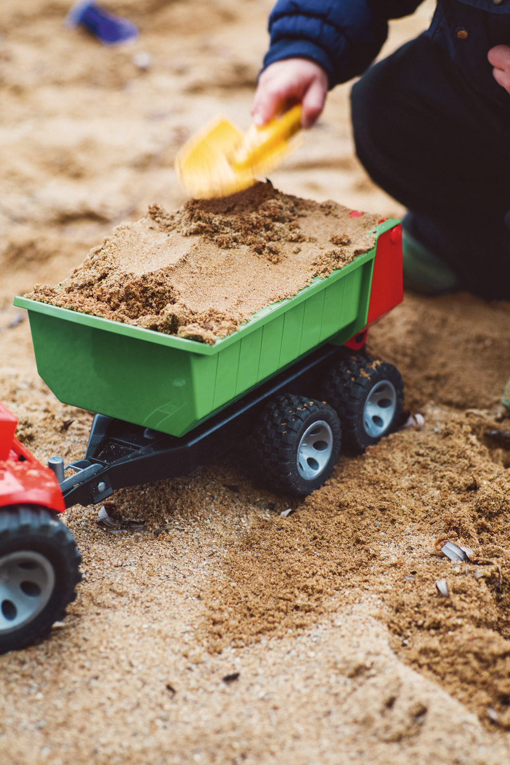 Kind spielt im Sandkasten mit Traktor und Anhänger, Anhänger ist mit Sand befüllt