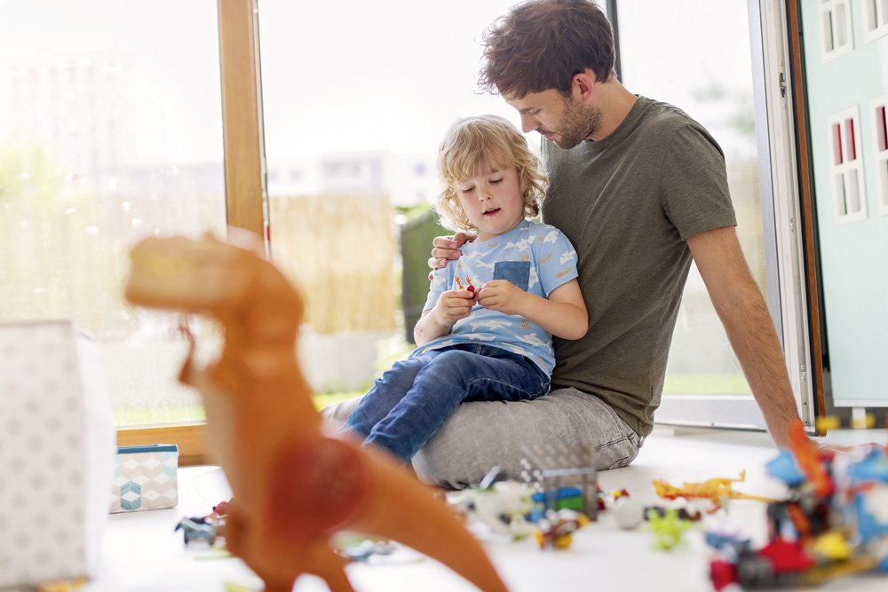 Kind sitzt mit Kindergärtner auf dem Boden und spielt mit Legofiguren 