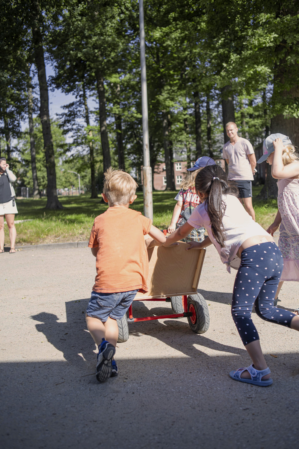 Kinder schieben Bollerwagen auf einem Weg im Grünen