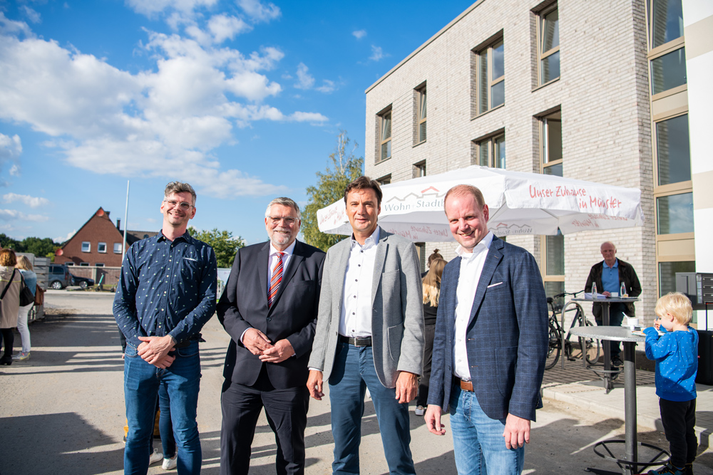 Vier Männer stehen vor einem Neubau und lächeln in die Kamera.