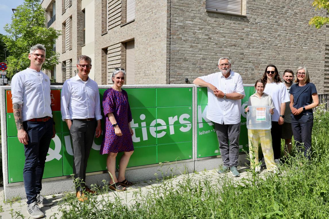 Eine Gruppe Menschen vor einer grünen Ausleihstation mit der Aufschrift „Quartierskiste“
